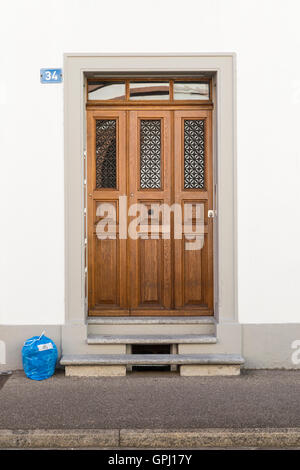 Frontansicht einer eleganten braunen Tür mit blauen Kennzeichen auf der linken Seitenwand und einen blauen Müllsack vorne auf dem Boden. Stockfoto