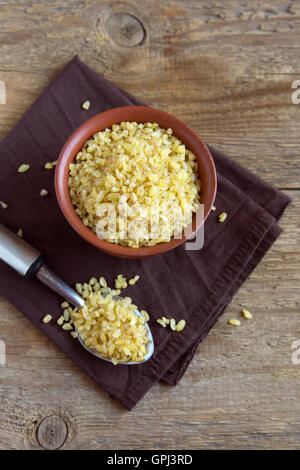 Bio Bulgur roh Weizenkorn in Keramikschale über rustikale Holz Hintergrund Stockfoto