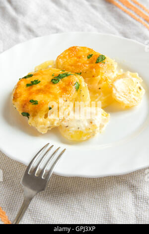 Kartoffel-Gratin (Eintopf) mit Sahne, Käse und Petersilie auf weißen Teller Stockfoto