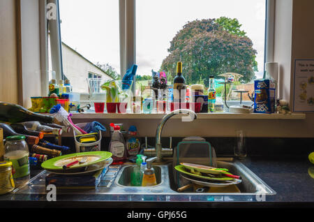 Ein Blick auf eine Küchewanne gefüllt mit schmutzigen Abwasch und das Küchenfenster mit Garten hinter. Stockfoto