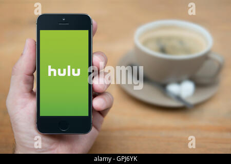 Ein Mann schaut auf seinem iPhone die die Hulu-video Abonnement-Logo anzeigt, während mit einer Tasse Kaffee (nur zur redaktionellen Verwendung) saß. Stockfoto