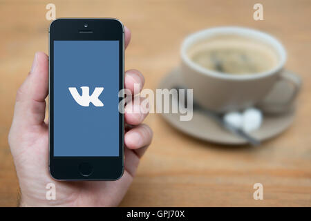 Ein Mann schaut auf seinem iPhone die das VK-russische social-Media-Logo anzeigt, während bei einer Tasse Kaffee (nur zur redaktionellen Verwendung) saß. Stockfoto