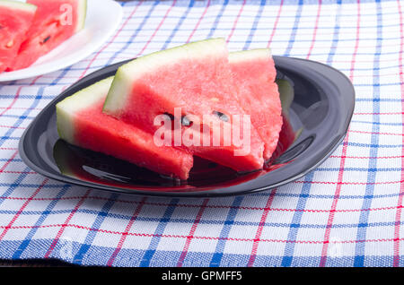 Seitenansicht der saftige rote Wassermelone Stücke auf einer schwarzen Platte auf eine Tischdecke Stoff mit flachen Schärfentiefe gemacht Stockfoto