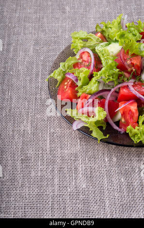 Fragment einer transparenten Platte mit einem frischen Salat von rohem Gemüse Nahaufnahme auf einer grauen Mat Tischplatte Stockfoto