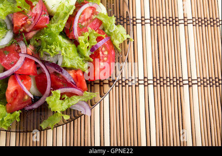 Detailansicht auf einem Fragment einer Platte mit frischen Salat aus rohen Tomaten, Salat und Zwiebel auf den Hintergrund Bambusmatte Stockfoto