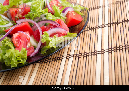 Nahaufnahme der Tischplatte mit einer braunen Bambusmatte und einen Teller frische vegetarische Salat Stockfoto