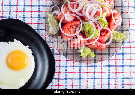 Draufsicht auf das natürliche hausgemachte Frühstück für eine Person - Spiegelei mit dem Eigelb und Tomaten Salat auf Stoff Tischdecke Stockfoto