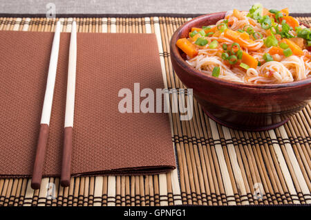 Reis Nudeln Hu-Teu mit Gemüse Karotte Sauce in einer kleinen braunen Holzschale auf einer gestreiften Matte in der Nähe von Stäbchen Stockfoto