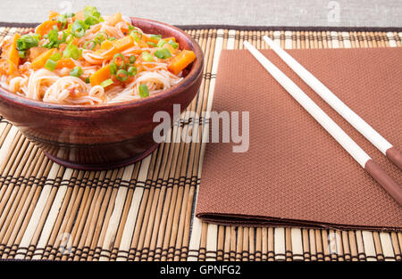 Reis Nudeln Hu-Teu mit Gemüse Karotte Sauce in einer kleinen braunen Holzschale auf einer gestreiften Matte in der Nähe von Stäbchen Stockfoto