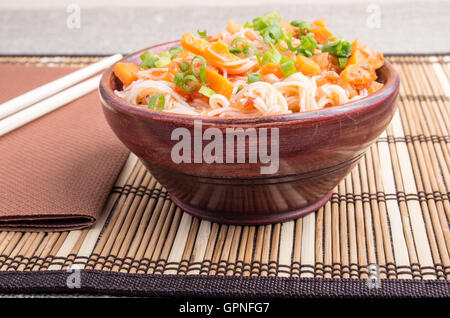 Kleine Portion Reis Vermicelli Hu-Teu mit Gemüse Karotte Sauce in einer kleinen braunen Holzschale auf einer gestreiften Matte in der Nähe von Ess-Stäbchen Stockfoto