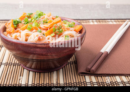 Kleine Portion Reis Vermicelli Hu-Teu mit Gemüse Karotte Sauce in einer kleinen braunen Holzschale auf einer gestreiften Matte in der Nähe von Ess-Stäbchen Stockfoto