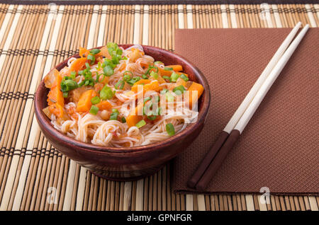 Eine Portion Reis Vermicelli Hu-Teu mit Gemüse Karotte Sauce in einer kleinen braunen Holzschale auf einer gestreiften Matte in der Nähe der hölzernen Stockfoto