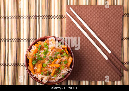 Draufsicht auf eine Portion Reis Vermicelli Hu-Teu mit Gemüse Karotte Sauce in einer kleinen braunen Holzschale auf einer gestreiften Matte in der Nähe von t Stockfoto