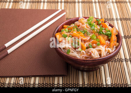 Eine Portion Reis Vermicelli Hu-Teu mit Gemüse Karotte Sauce in einer kleinen braunen Holzschale auf einer gestreiften Matte in der Nähe der hölzernen Stockfoto