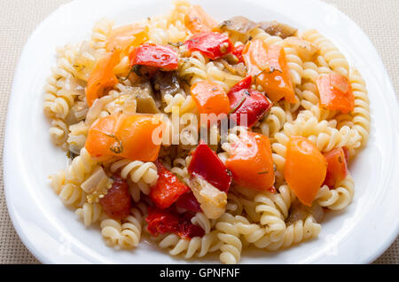 Italienische Nudeln Fusilli mit Gemüseragout von Paprika und gedünstetem Gemüse auf einem weißen Teller Nahaufnahme auf Stoff Hintergrund Stockfoto