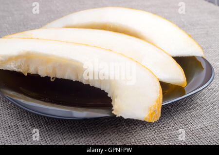 Gesunde und natürliche Stücke von gelber Melone auf einer schwarzen Platte auf Stoff-Hintergrund Stockfoto