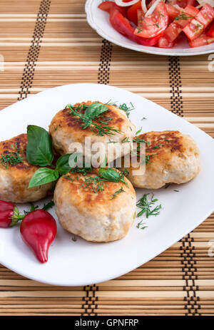 Gesunde Hausmannskost, hergestellt aus natürlichen Zutaten - Hähnchen Frikadellen von Hackfleisch / Faschiertem und einem Salat aus rohen Tomaten auf einem gestreiften Stockfoto