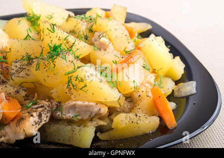 Scheiben von der geschmorten Kartoffeln, Huhn, Karotten und Zwiebeln bestreut mit Gewürzen und grünen Dill auf einer schwarzen Platte-Nahaufnahme Stockfoto