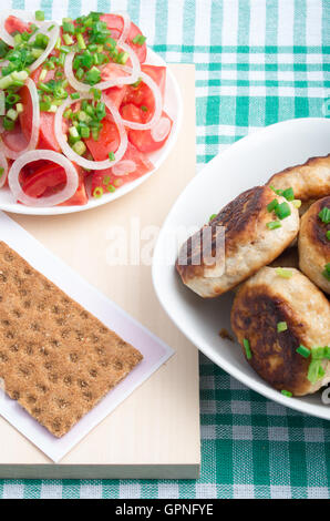 Hausgemachte gebratene Fleischbällchen in einer Schüssel weiß, Salat von rohem Gemüse und Vollkorn Zwieback auf einer grünen Tischdecke Stockfoto