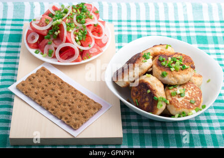 Draufsicht auf hausgemachte gebratene Fleischbällchen in einer Schüssel weiß, Salat von rohem Gemüse und Vollkorn Zwieback auf einer grünen Tischdecke Stockfoto