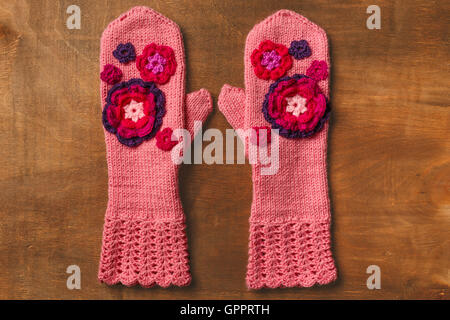 Rosa gestrickte Handschuhe mit Blumen auf hölzernen Hintergrund Stockfoto