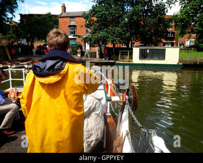 Ein Mann in einem gelben Mantel betreibt eine handbetriebene Kette Fähre über einen Fluss in Stratford. Stockfoto