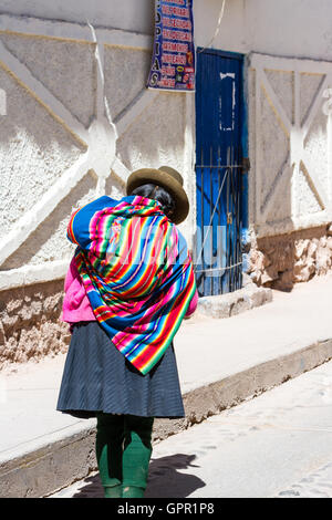 Maras Peru-Mai 18: einheimische Quechua-Frau mit schönen Farben, die zu Fuß in Richtung einer blauen Tür. 18. Mai 2016, Maras Peru. Stockfoto