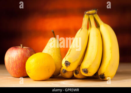 Obst auf dem Tisch - Bananen Birne Apfel und Zitrone auf einem Schreibtisch aus Holz Stockfoto