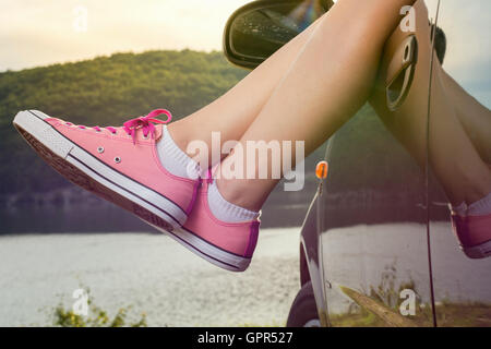 Frau Beine aus dem Autofenster am See Stockfoto