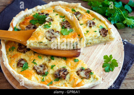 Hausgemachte französische Quiche Kuchen mit Pilzen (Champignons) und Käse über rustikale Holz Hintergrund Stockfoto