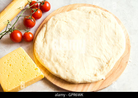 Den Teig auf Schneidebrett, Tomaten und Käse für Pizza über weißen Tisch Stockfoto