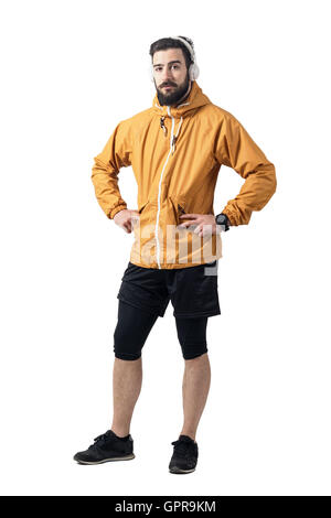 Jogger in Sportjacke mit Blick in die Kamera im akimbo Pose Kopfhörer. Ganzkörper-Länge-Porträt isoliert auf weisse studio Stockfoto