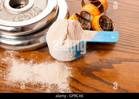 Molke-Protein-Pulver in Mess-Schaufel, m-Band und Hantel auf hölzernen Hintergrund. Stockfoto