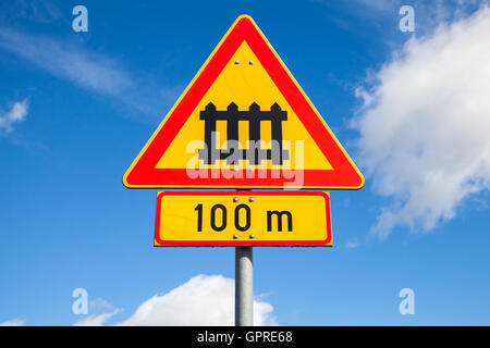 Schweden-Bahnübergang mit Tor Zeichen. Dreieckige Warnung Roadsign mit roten Rand und 100m Entfernung-Etikett über blauen Wolkenhimmel Stockfoto