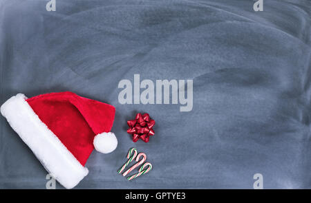 Santa Cap, Geschenk Bogen und Candy Canes auf gelöschte Tafel für Weihnachts-Wunschliste-Konzept. Stockfoto
