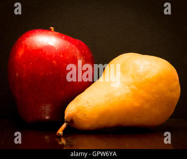 Einen leckeren roten Apfel und eine braune Bosc Birne auf einem schwarzen Hintergrund. Stockfoto