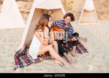 Lockigen Jüngling Gitarre für seine Freundin sitzen am camping Zelt Stockfoto