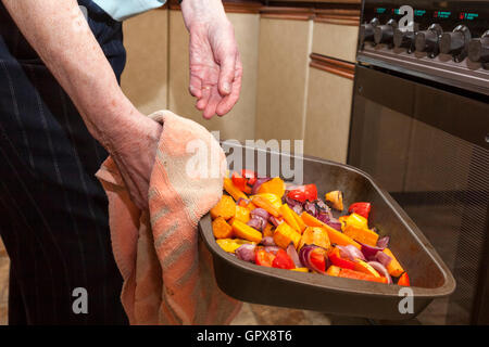 Ältere Person zu Hause kochen. Ältere Frau mit einem Bräter aus gerösteten Gemüse gerade aus dem Ofen genommen Stockfoto