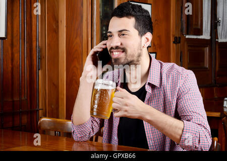 Porträt des Jünglings Latein sprechen am Telefon mit Glas Bier und Snacks in der Bar. Im Innenbereich. Stockfoto