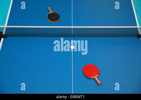 Tischtennisschläger blau rot und schwarz und eine Kugel auf eine Tischtennisplatte, Ansicht von oben Stockfoto