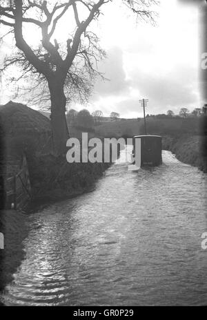 1938, macht historische, kleine Lieferwagen seinen Weg durch das Wasser auf überfluteten Landstraße in der Nähe von Chagford, Devon, England, die am Rande des Dartmoor National Park und ist nah an dem Fluß Teign. Stockfoto