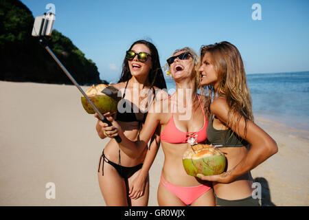 Gruppe der glückliche junge Frau mit Kokosnüssen Selfie am Strand nehmen. Drei junge Frauen im Bikini am Meer Shire unter selbst po Stockfoto