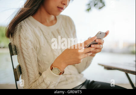 Schuss von Weibchen mit Handy in Straßencafé beschnitten. Junge Frau liest SMS-Nachricht auf ihr Smartphone. Stockfoto