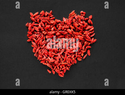 Rohe getrocknete Goji-Beeren in Form eines Herzens auf einem schwarzen Hintergrund angeordnet Stockfoto