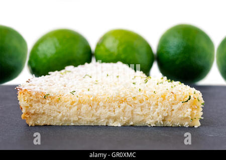 Zitrone, Limette, Kokosnuss unmöglich Torte mit weißer Schokolade Späne Slice auf einem grauen Schiefer mit Limetten im Hintergrund Stockfoto