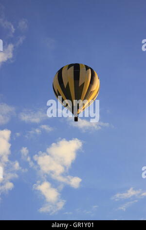 Heißluft-Ballon, gelben und schwarzen Streifen, Montgolfier Flug gegen blauen Himmel, weiße Wolken Stockfoto