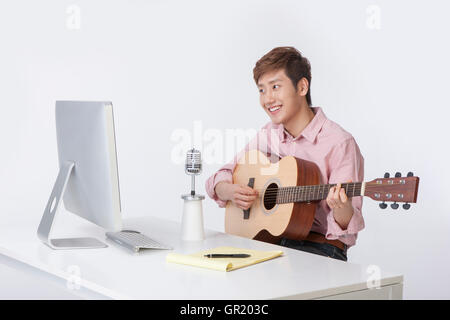Junger lächelnder Mann, eine Gitarre mit Computer und Mikrofon Stockfoto