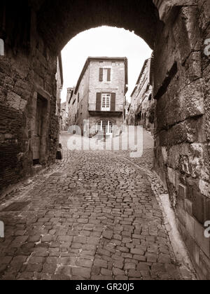 A Straße Divided Monochrom. Eine gepflasterte Straße ergibt sich aus einem Stadttor und teilt sich dann auf und ab Hügel mit einem engen Haus Stockfoto