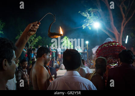Ein Mann hält eine Flamme aloft, die Verfahren in ein Theyyam Ritual in einem nördlichen Keralas Dorf in der Nähe von Kannur zu beleuchten Stockfoto