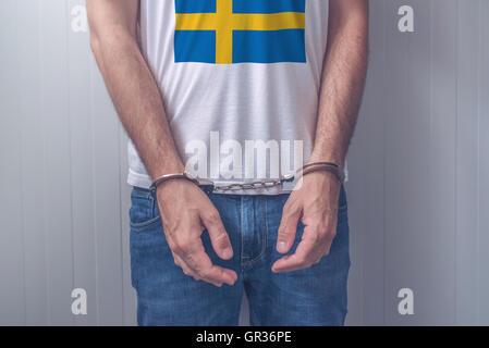 Mann mit gefesselten Händen tragen Hemd mit schwedischen Flagge verhaftet. Nicht erkennbare männliche Person in Jeans mit Handschellen Stockfoto